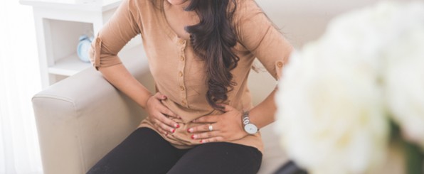 痛みにお腹をおさえる女性